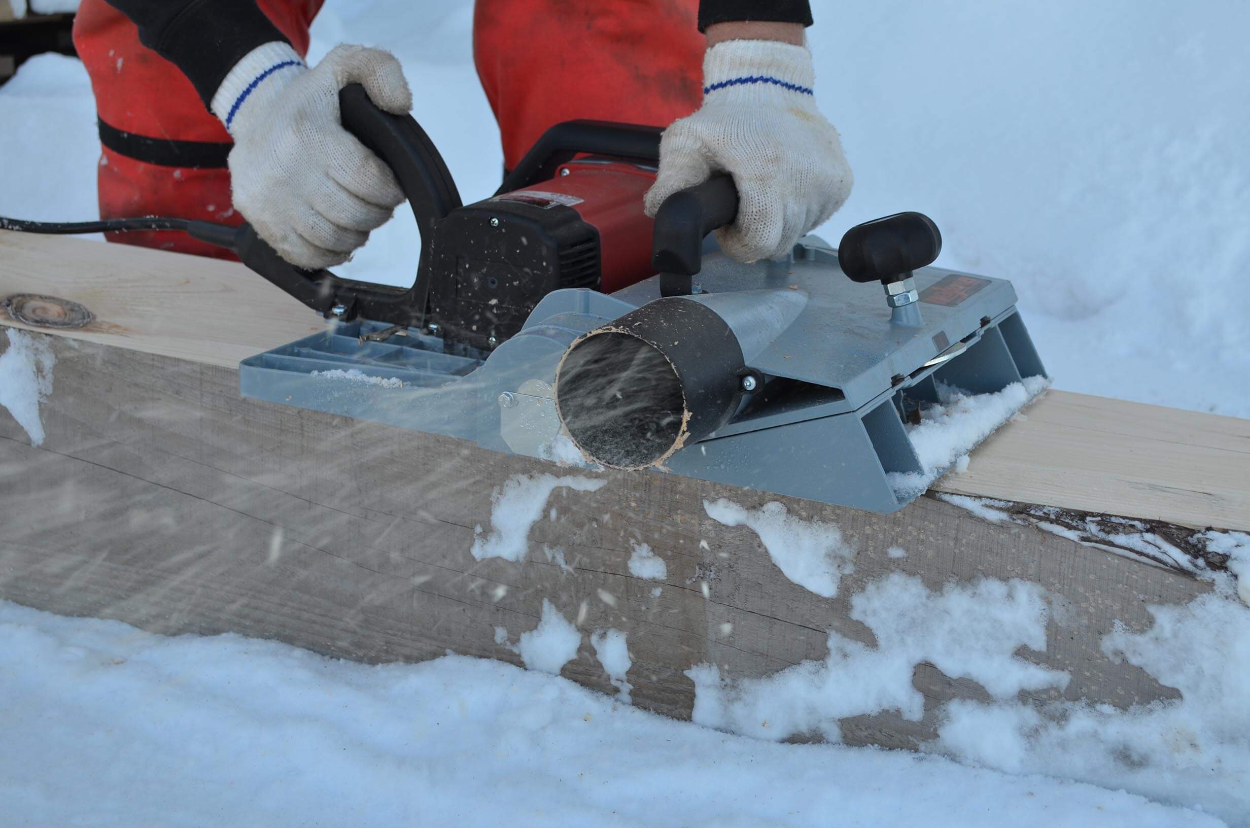 Close up of hands planing the wood in the snow.