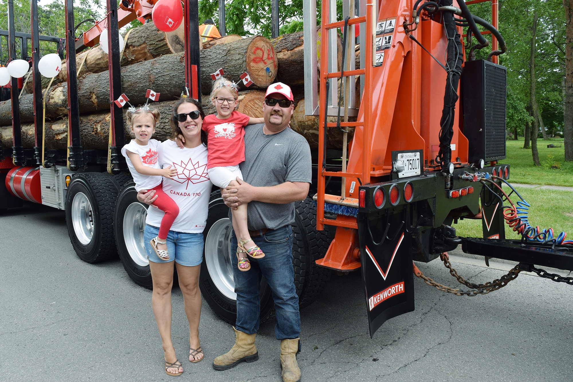 Man and women with 2 girls standing in front of Townsend lumber truck covered in red and white balloons for Canada Day.