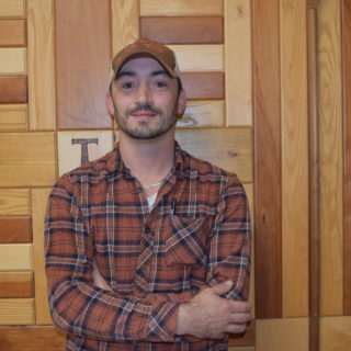 Headshot of Daryl Mason standing in front of a wooden wall.