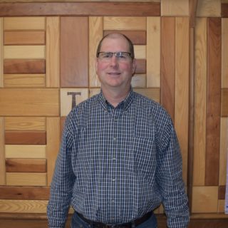 Headshot of Mac Troyer standing in front of a wooden wall.