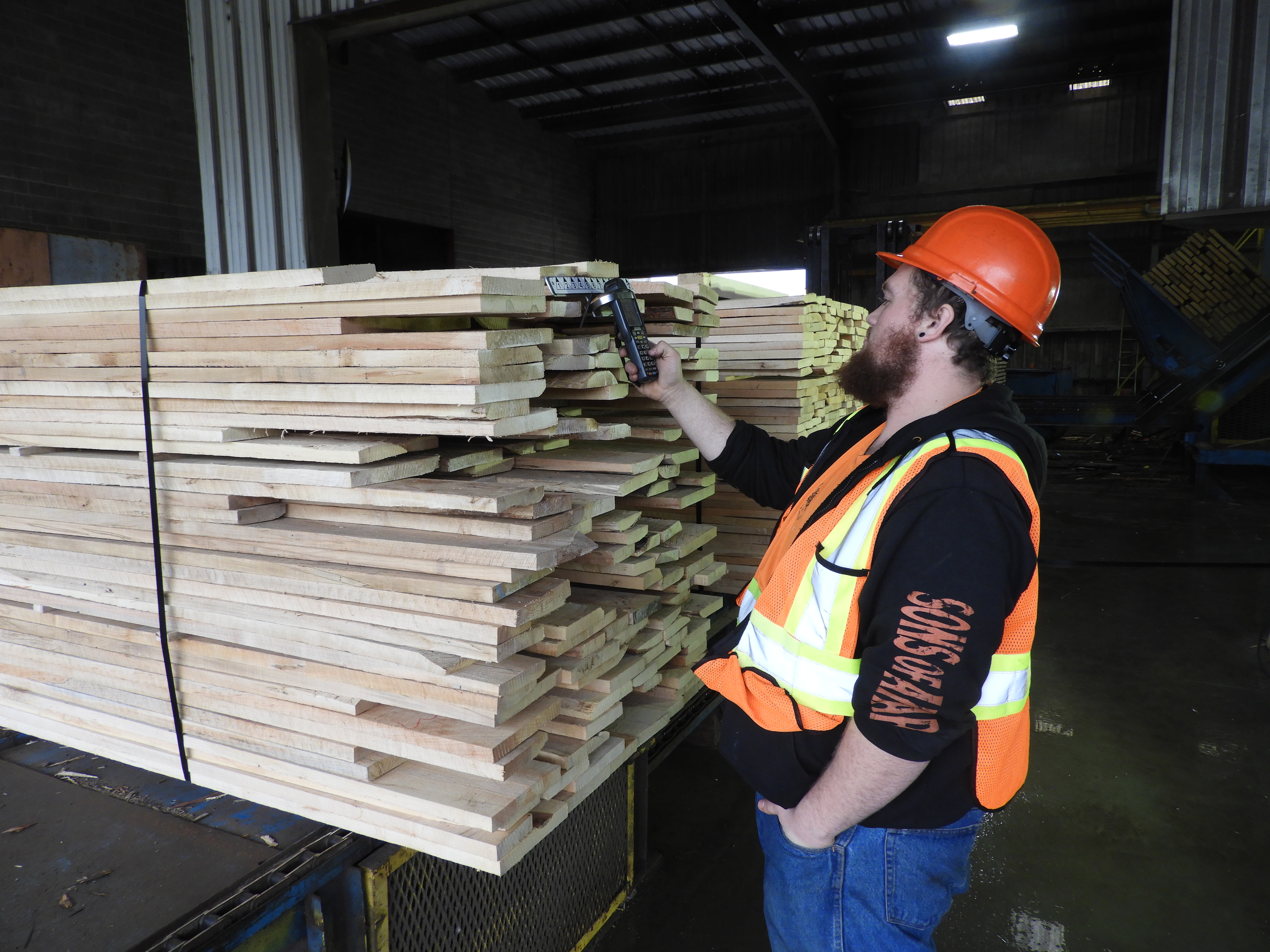 Man in construction uniform inspecting stacks of wood in wearhouse.