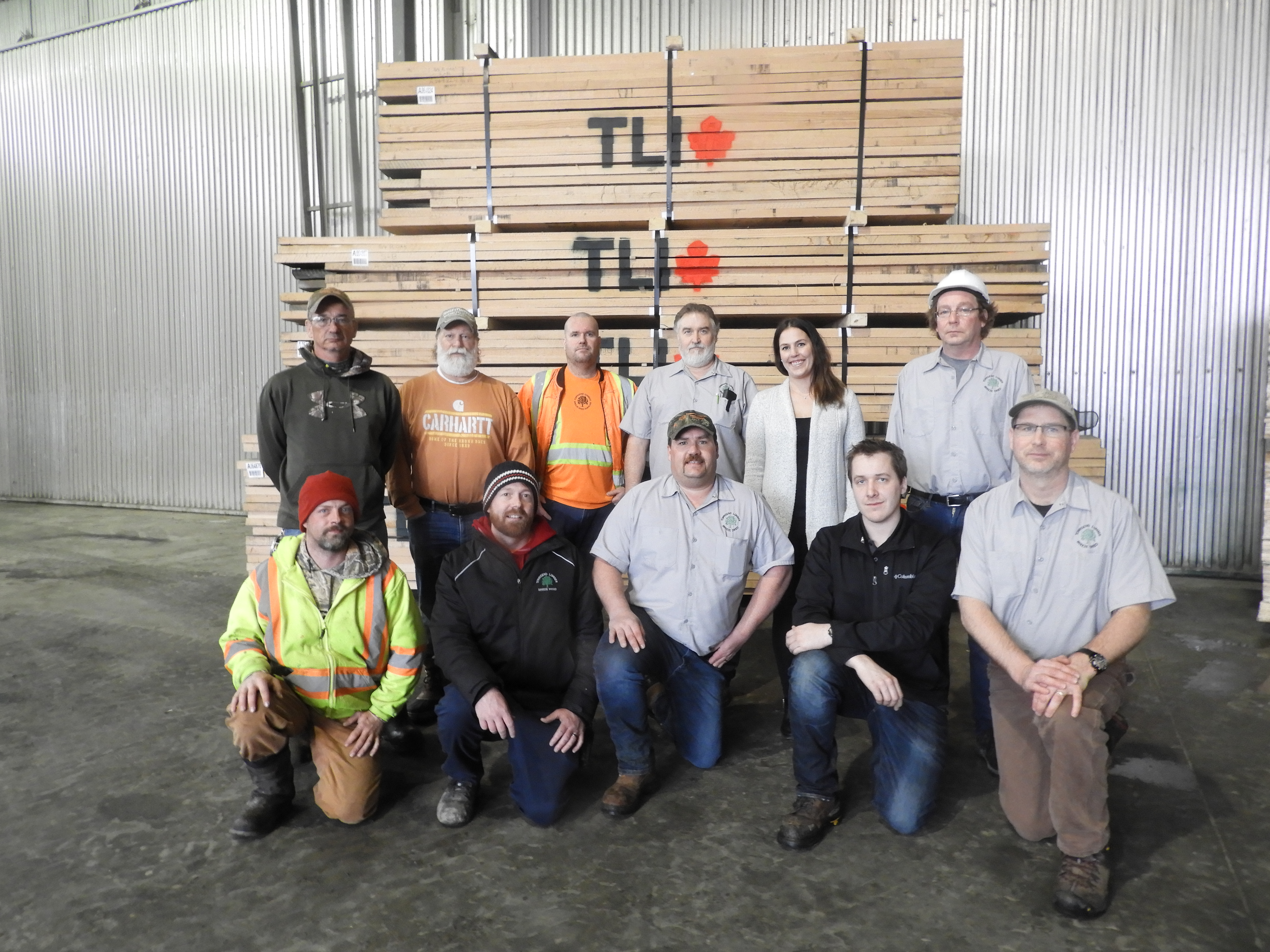 11 staff members posing in front of large pallet of wood with the TLI logo on it.