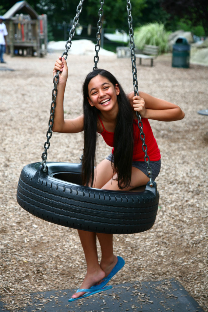 Young girl smiling, sitting on a tire swing at playground.