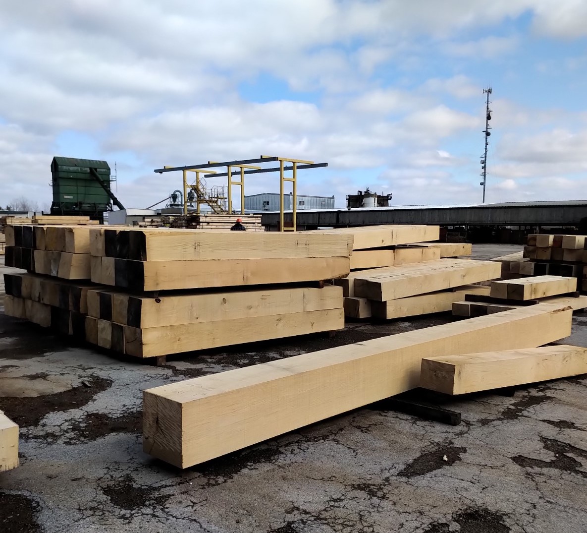 Large blocks of wood sitting in a concerte lot with machines in background.