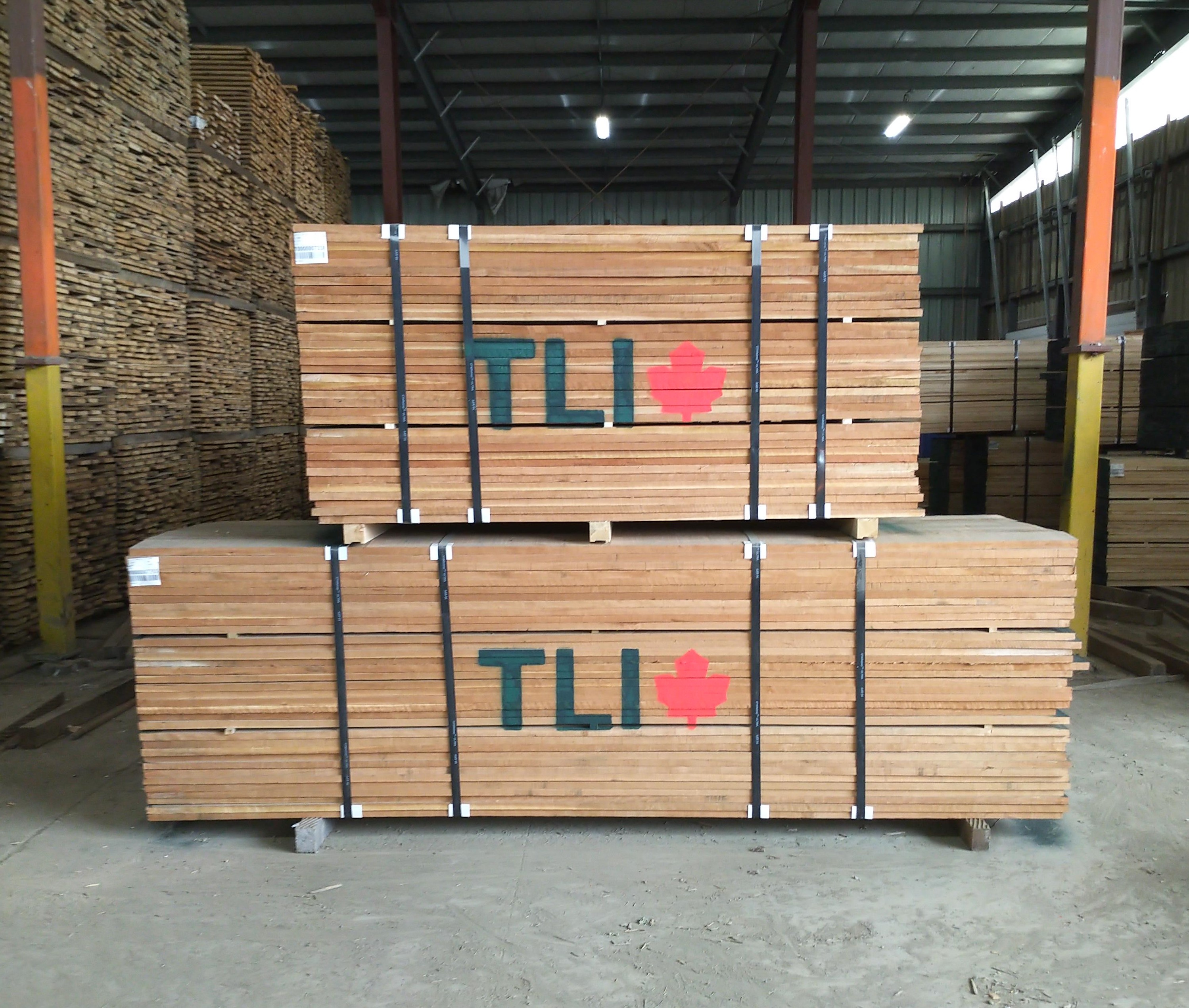 Large pallets of wood with the TLI logo painted on the side are sitting inside of a wearhouse