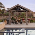 Wooden pergola with chairs and table next the swimming pool. Picture taken at dusk.