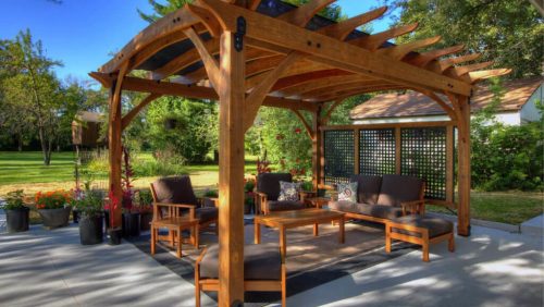 Porter-1024x684_pergola3 Wooden pergola with chairs and table next to a shed and large grass field. Picture taken on a sunny day.