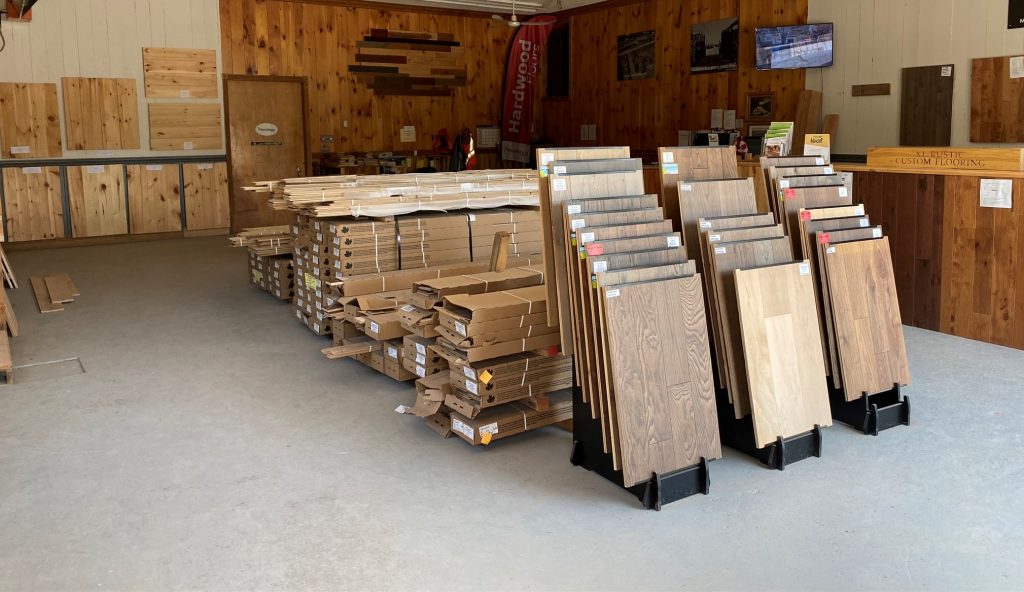 Inside a building, hardwood samples are displayed on the walls and boxes of wood are in the middle of the room.