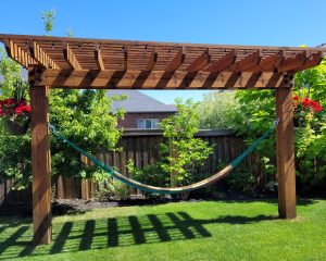 A narrow wooden structure with two posts and a slatted roof with a hammock strung up between the posts.