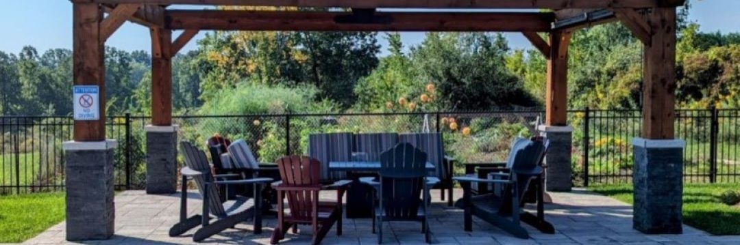 A wooden pergola with seating underneath stands near a swimming pool, with lush greenery in the background.